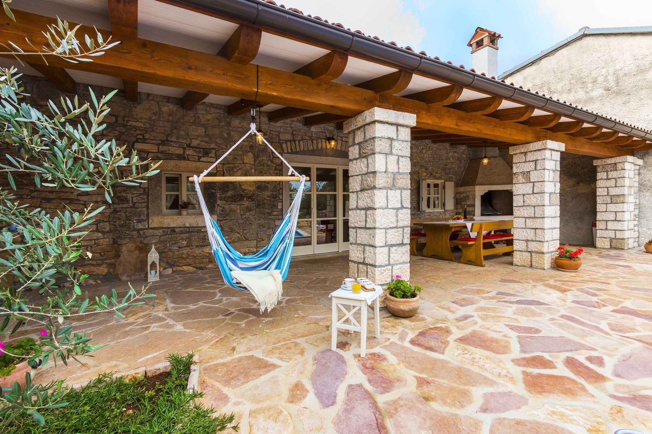 A stone patio with a hammock, outdoor seating, and a stone fireplace.