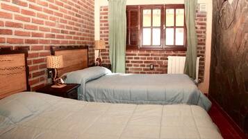 A room with two beds, a brick wall, a window with shutters, and a radiator.