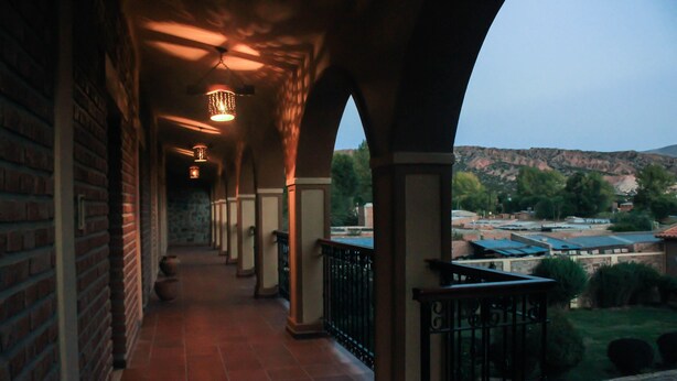 A covered corridor with brick walls and a tiled floor, leading to a balcony with a view of a hilly landscape. - Hosteria Del Inca (Humahuaca)