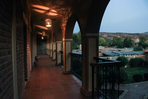 Ein überdachter Gang mit Backsteinwänden und Fliesenboden, der zu einem Balkon mit Blick auf eine hügelige Landschaft führt.