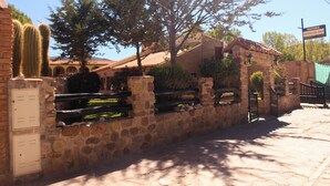 A stone wall with a cactus, a tree, and a building with a tiled roof. - Hosteria Del Inca (Humahuaca)