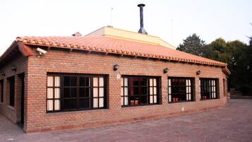 A brick building with a tiled roof, large windows, and a chimney.