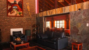 A cozy living room with a black leather sofa, a wooden coffee table, and a brick wall with a mural. - Hosteria Del Inca (Humahuaca)