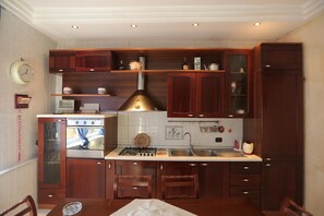 Een keuken met houten kastjes, een fornuis, een spoelbak en een klok aan de muur.