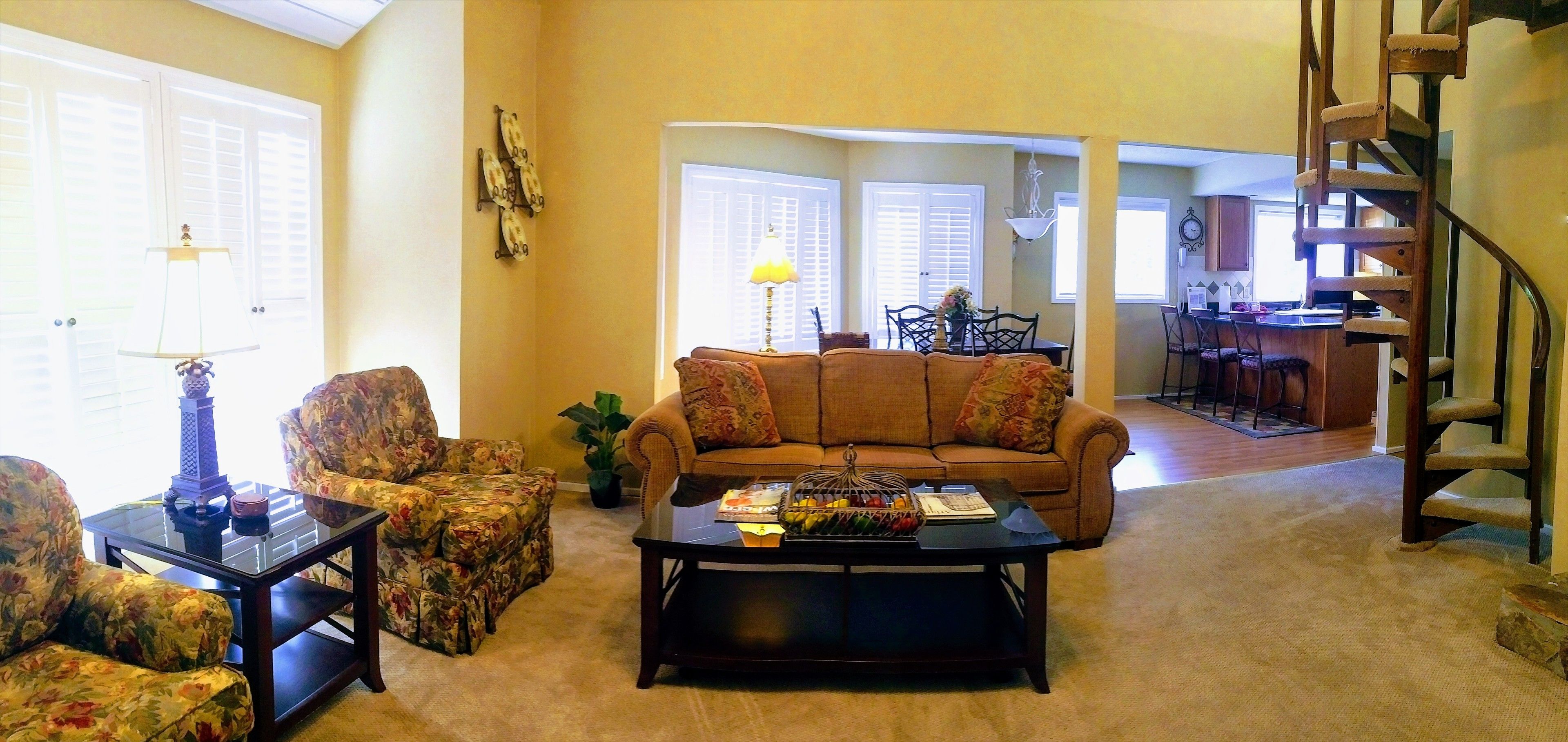 A living room with a sofa, armchairs, a coffee table, and a staircase.