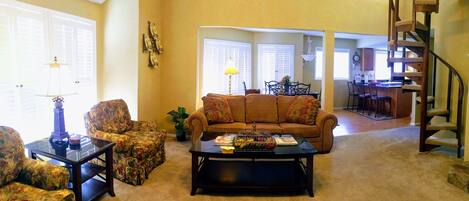 A living room with a sofa, armchairs, a coffee table, and a staircase.