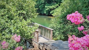 A wooden bridge over a calm river, surrounded by lush greenery and pink flowers. - Fairfield Plantation Resort (Villa Rica)