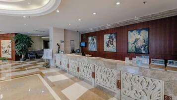 A hotel reception area with a marble floor, a reception desk with a decorative railing, and artwork on the walls.