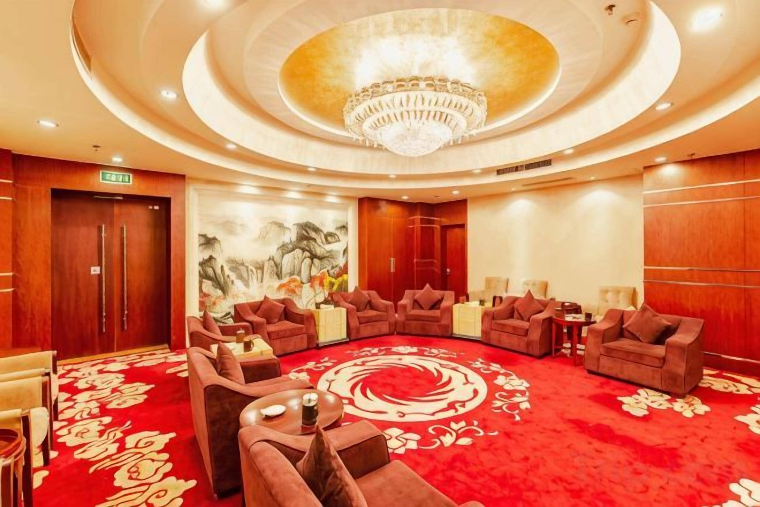 A hotel lobby with a circular seating area, a chandelier, and a red carpet.