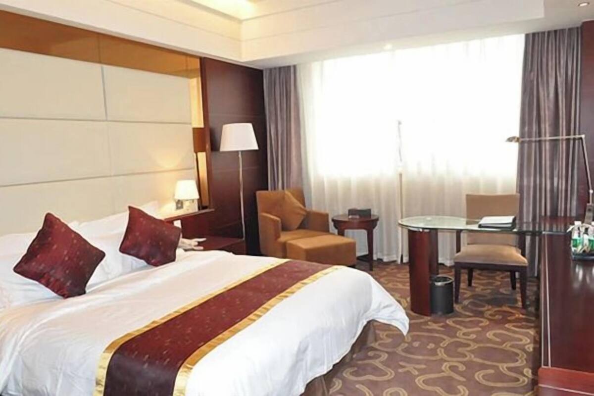 A hotel room with a large bed, a desk, a chair, a lamp, and a view of the outdoors.