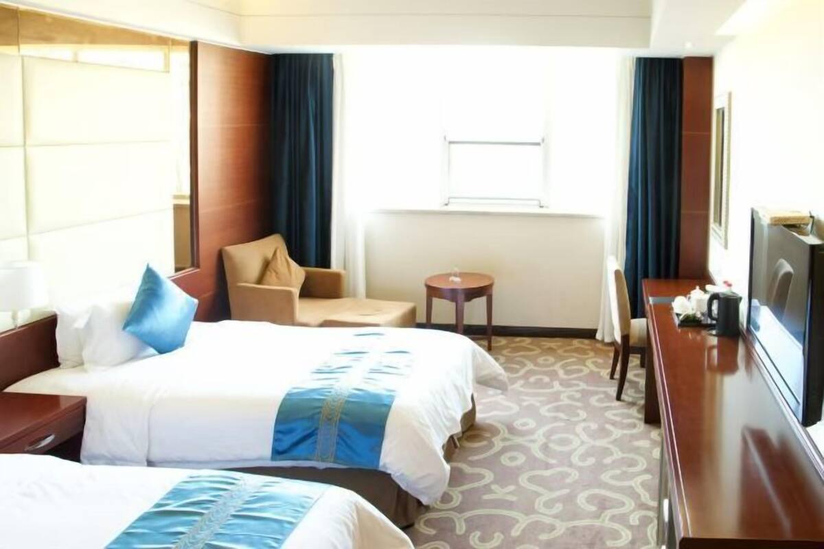 A hotel room with two beds, a desk, a chair, a small table, and a TV.
