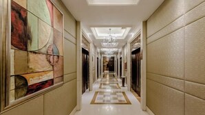 Un pasillo de hotel con piso a cuadros, un candelabro y un cuadro abstracto grande en la pared izquierda.