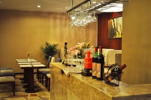 Una zona de bar con mostrador de mármol, botellas de vino, copas y un jarrón decorativo con flores.