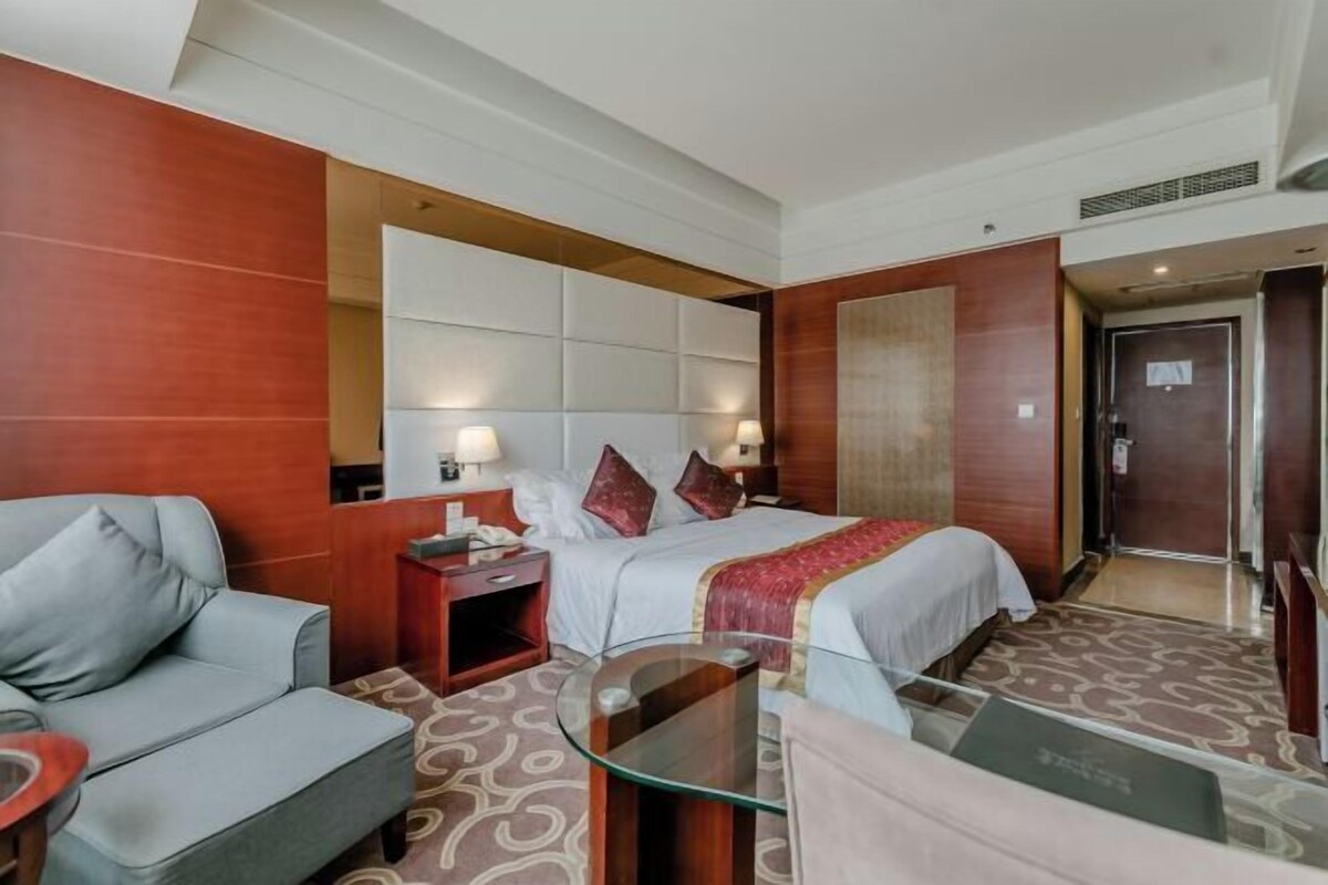 A hotel room with a bed, a sofa, a glass table, and a nightstand.