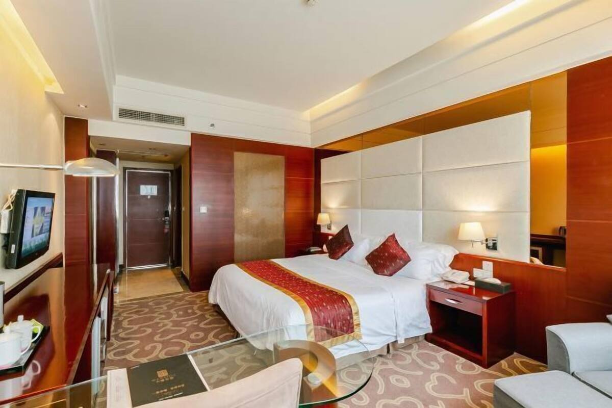 A hotel room with a bed, bedside tables, a TV, and a glass coffee table.