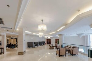 Un hall d’entrée spacieux avec un plafond haut, des lustres et un espace détente comprenant des canapés et des fauteuils.