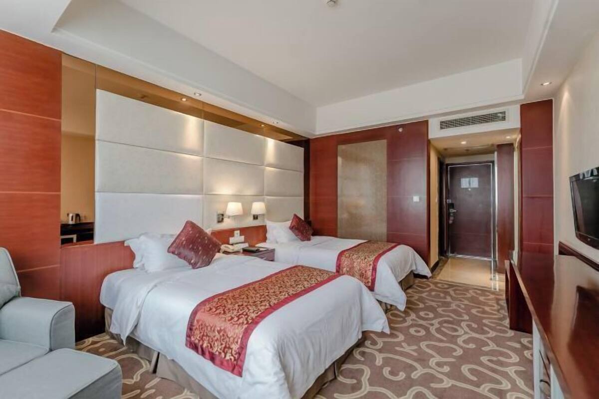 A hotel room with two beds, a sofa, a TV, and a large mirror.