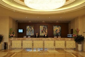A hotel reception area with a reception desk, two receptionists, a large chandelier, and artwork on the wall. - Qingshen Hotel (Qingshen)