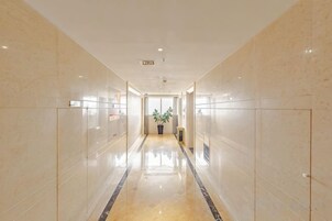 Un pasillo largo y estrecho con pisos y paredes reflectantes, que conduce a una habitación con una planta y una puerta al final.