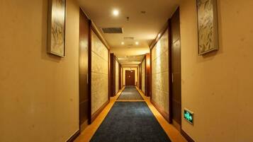 A hotel corridor with doors on both sides, a carpeted floor, and a light switch on the wall.