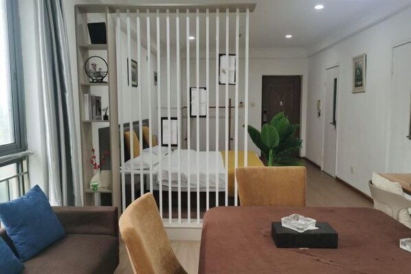 A modern living room with a brown sofa, a dining table with a glass centerpiece, and a white partition with shelves. - Langfei Business Hotel (Chongqing)