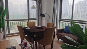 Ein modernes Wohnzimmer mit Esstisch, Stühlen, einer Couch und großen Fenstern mit Blick auf die Stadt.