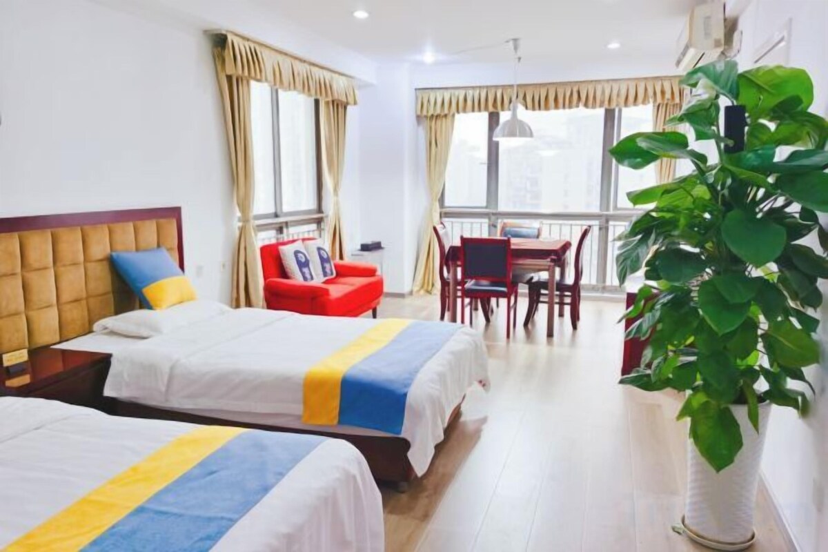 A hotel room with two beds, a dining table, chairs, and a large potted plant.