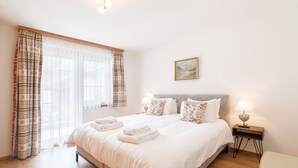 A neatly made bed with white linens and folded towels, a bedside table with a lamp, and a painting on the wall. - Chalet Ulysse Zermatt 4 guests /cosy/private garden/beautiful (Zermatt)