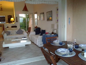 Uma sala de estar com sofá, mesa de jantar posta com pratos e copos, e uma cadeira.