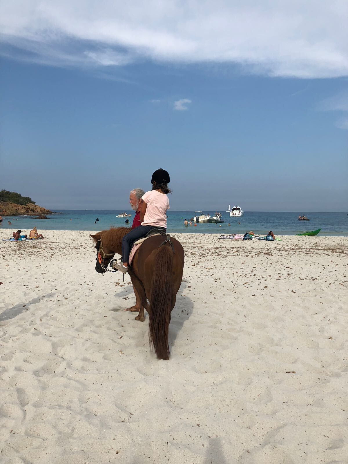 A beach scene with a horse and rider, boats, and people in the water.