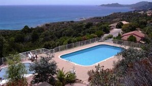 A rectangular swimming pool with a surrounding deck, set against a backdrop of a coastal landscape and distant hills.
