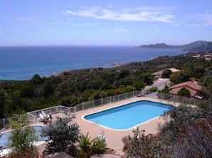 Piscina retangular com um deck ao redor, com paisagem costeira e colinas ao fundo.