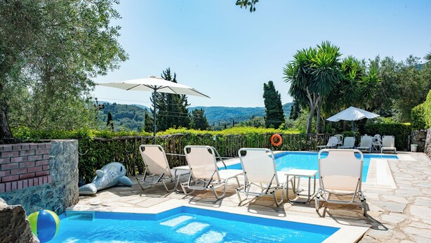A swimming pool with lounge chairs and umbrellas, surrounded by greenery and a view of hills. - Stathis House - Ag. Georgios Corfu (Pagi)