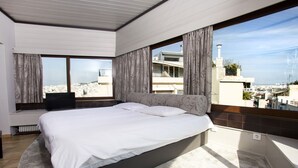 Ein Schlafzimmer mit einem großen Bett, einem Fernseher und Blick auf die Stadt durch große Fenster.