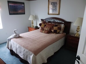 Een net opgemaakt bed met een zwanendecoratie, een geborduurde spreideken en meerdere kussens. Er staan twee nachtkastjes met lampen en een ingelijst schilderij aan de muur.