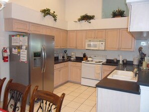 A kitchen with a refrigerator, microwave, stove, and sink. There are cabinets, chairs, and a fire extinguisher. - Our Home from Home Villa  Maximum occupancy is 8 people (Davenport)