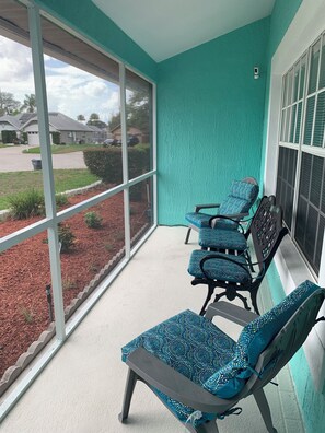A balcony with four chairs and a table, large windows, and a view of a residential area. - Our Home from Home Villa  Maximum occupancy is 8 people (Davenport)