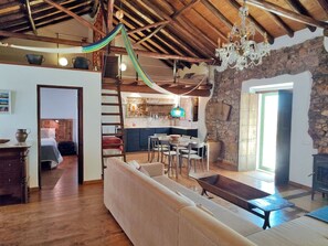 A spacious living area with a wooden ceiling, a stone wall, and a dining area with a table and chairs.