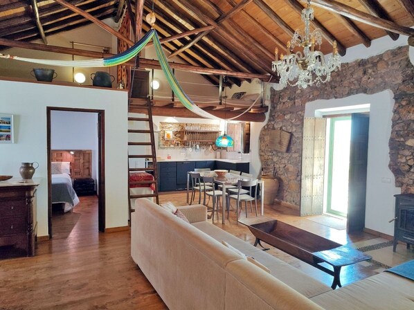 A spacious living area with a wooden ceiling, a stone wall, and a dining area with a table and chairs.