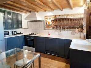 A modern kitchen with dark cabinets, a glass table, and a stone backsplash.