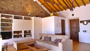 Amplia sala de estar con techo de madera alto, un sofá grande, estanterías blancas empotradas y una pared de piedra.