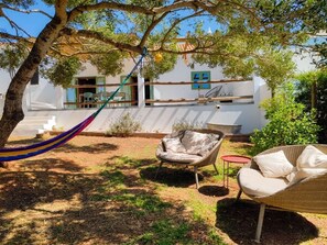 A garden with a hammock, wicker chairs, and a white building with a balcony.