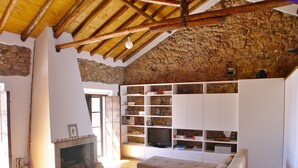 Un salón rústico con pared de piedra, vigas de madera, chimenea, sofá y estanterías empotradas.