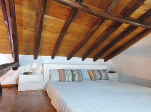 A bedroom with a wooden ceiling, a bed with striped pillows, a bedside table with a lamp, and a white nightstand.