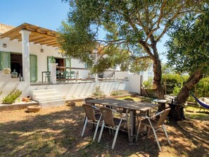 A patio with a table and chairs, a hammock, and a large tree.