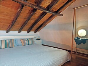 A bedroom with a sloped ceiling, a bed with striped bedding, a bedside table with a lamp, and a round mirror on the wall.