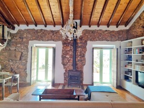 A cozy living room with a stone wall, a fireplace, a wooden ceiling, and a bookshelf.