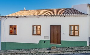 A white building with a green base, a tiled roof, and a wooden door.