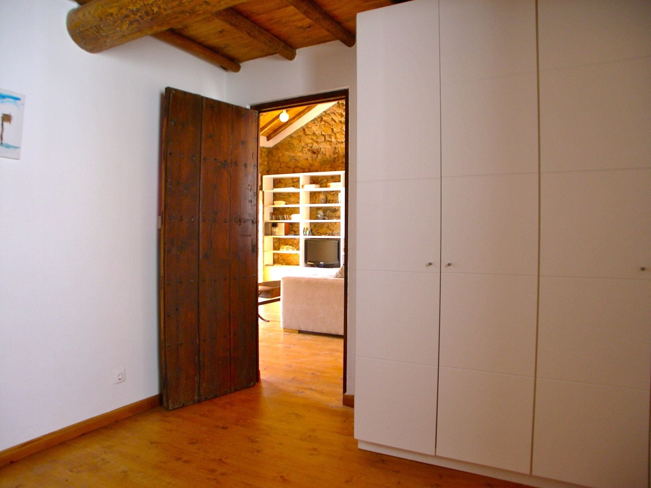 Ein Zimmer mit einer Holztür, einem weißen Kleiderschrank und einer Steinwand im Hintergrund.