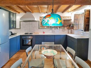 Eine moderne Küche mit blauen Schränken, einer Holzbalkendecke und einem Glastisch mit Stühlen.